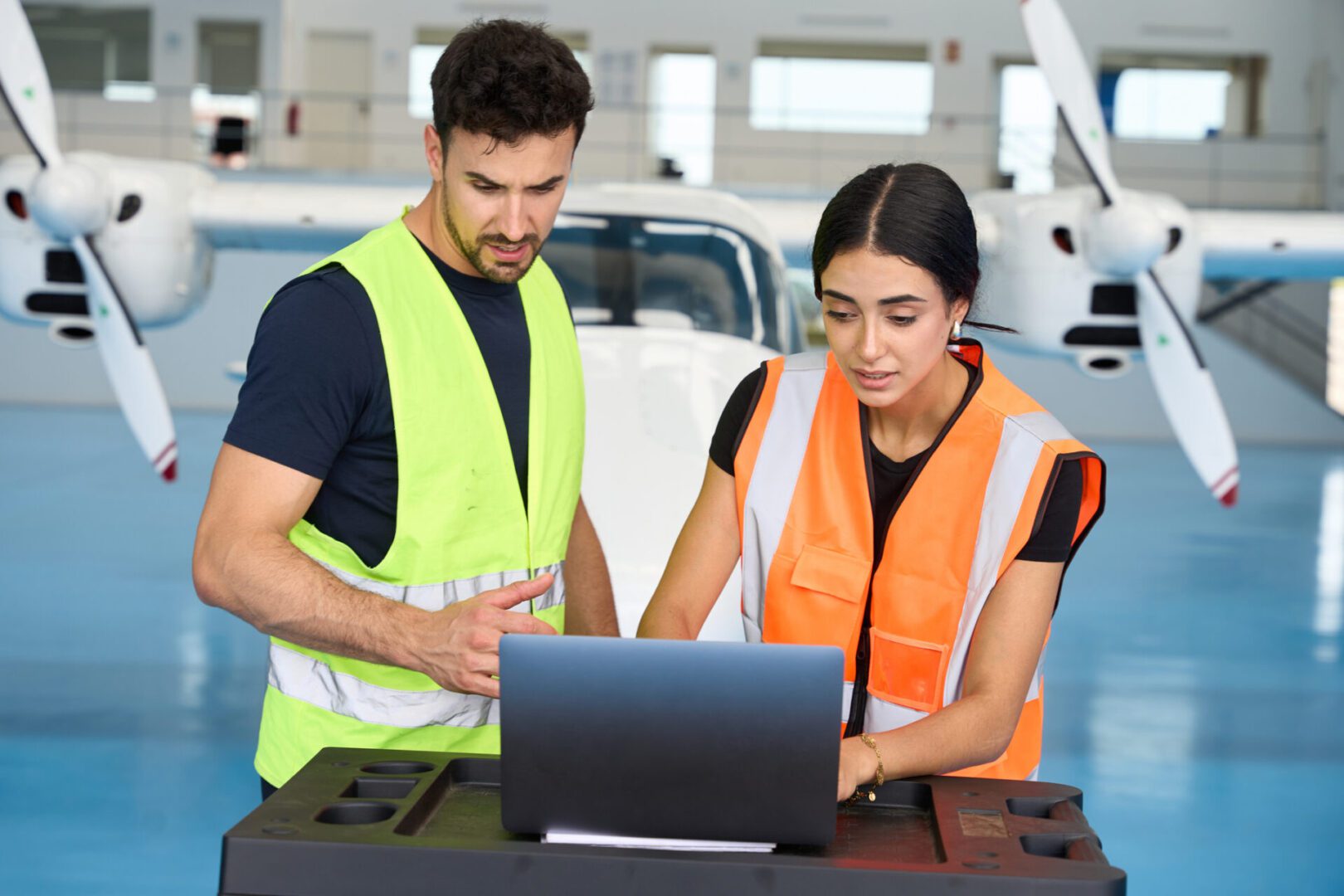 Two technicians working on laptop near airplane.