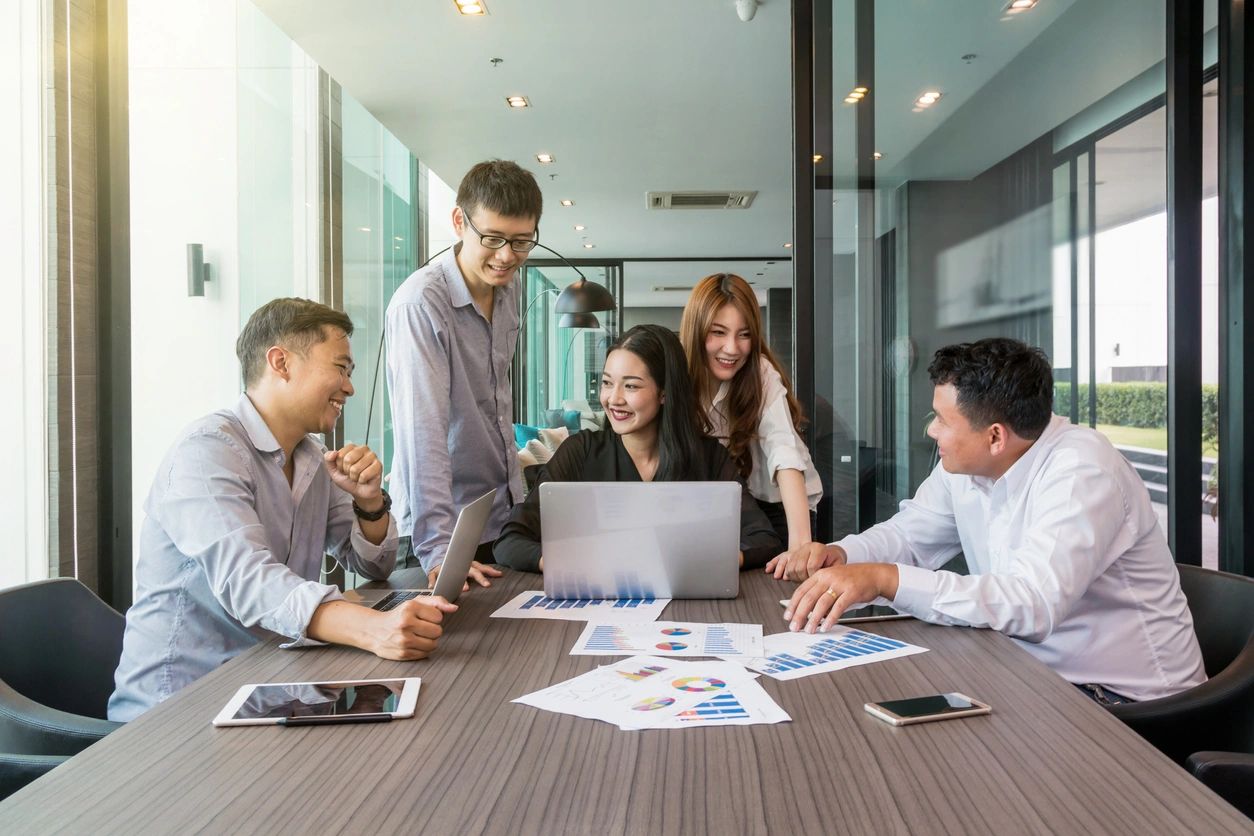 A group of young professionals collaborating around a laptop in a modern office.