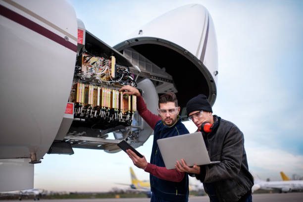 Two technicians inspect an open aircraft engine with a laptop.